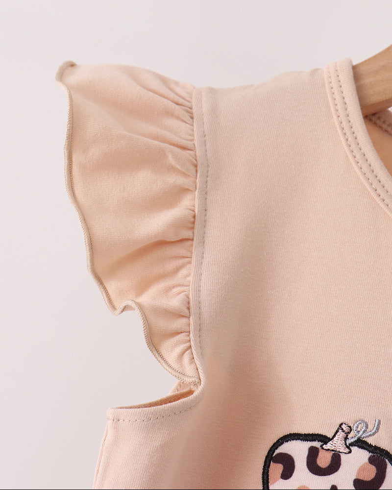 Close-up of a light peach sleeveless top with ruffled shoulder details and a partial cartoon graphic at the bottom, shown against a plain light background.