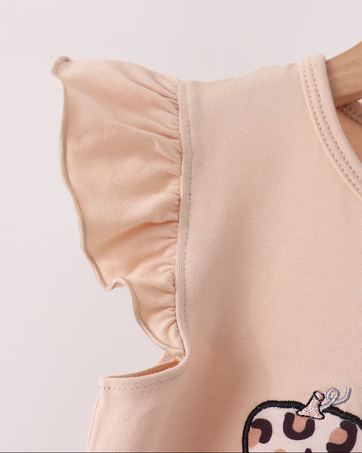 Close-up of a light peach sleeveless top with ruffled shoulder details and a partial cartoon graphic at the bottom, shown against a plain light background.