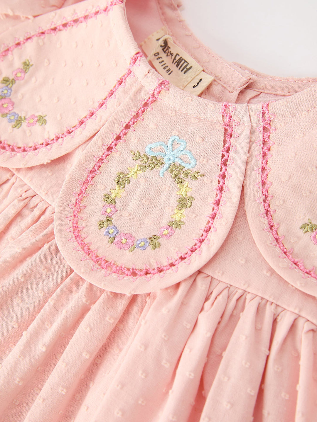 Pink dress closeup: round floral embroidery on yoke with ruffled trim