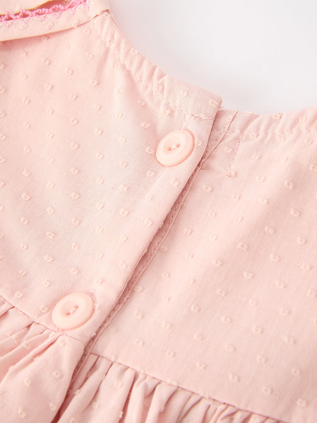 Pink dress bodice closeup with button placket and textured dot fabric, ruffled waist