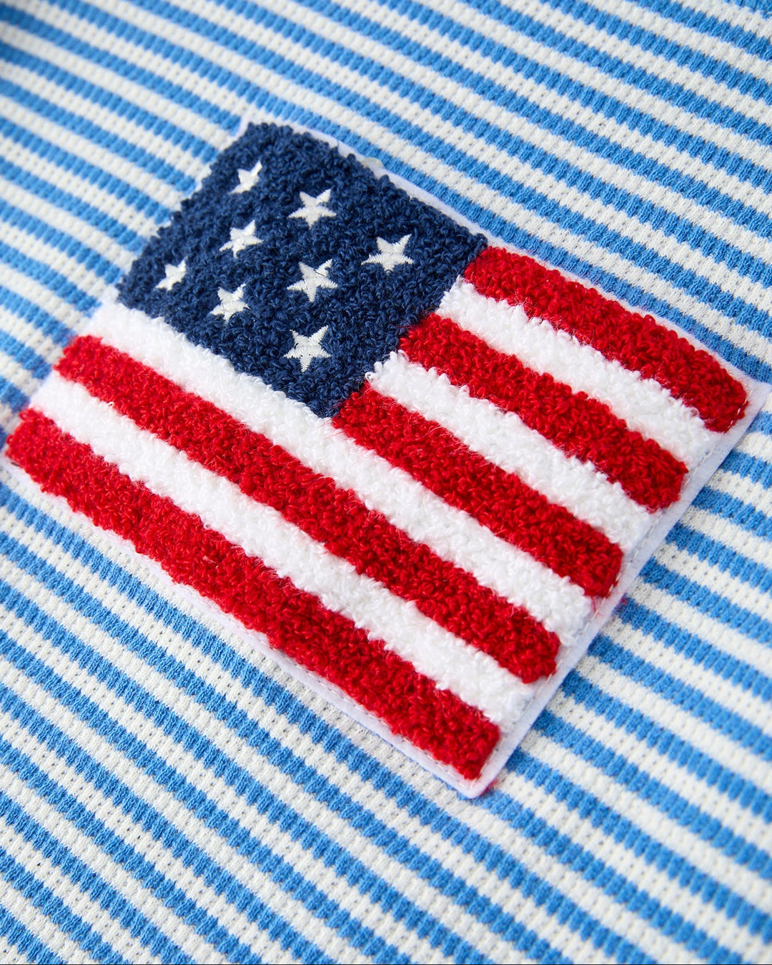 Embroidered American flag patch on a blue and white striped fabric background