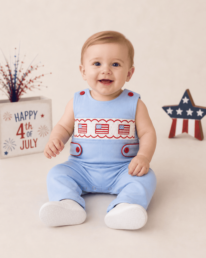Baby wearing a blue outfit with American flag design, sitting on a white surface with &