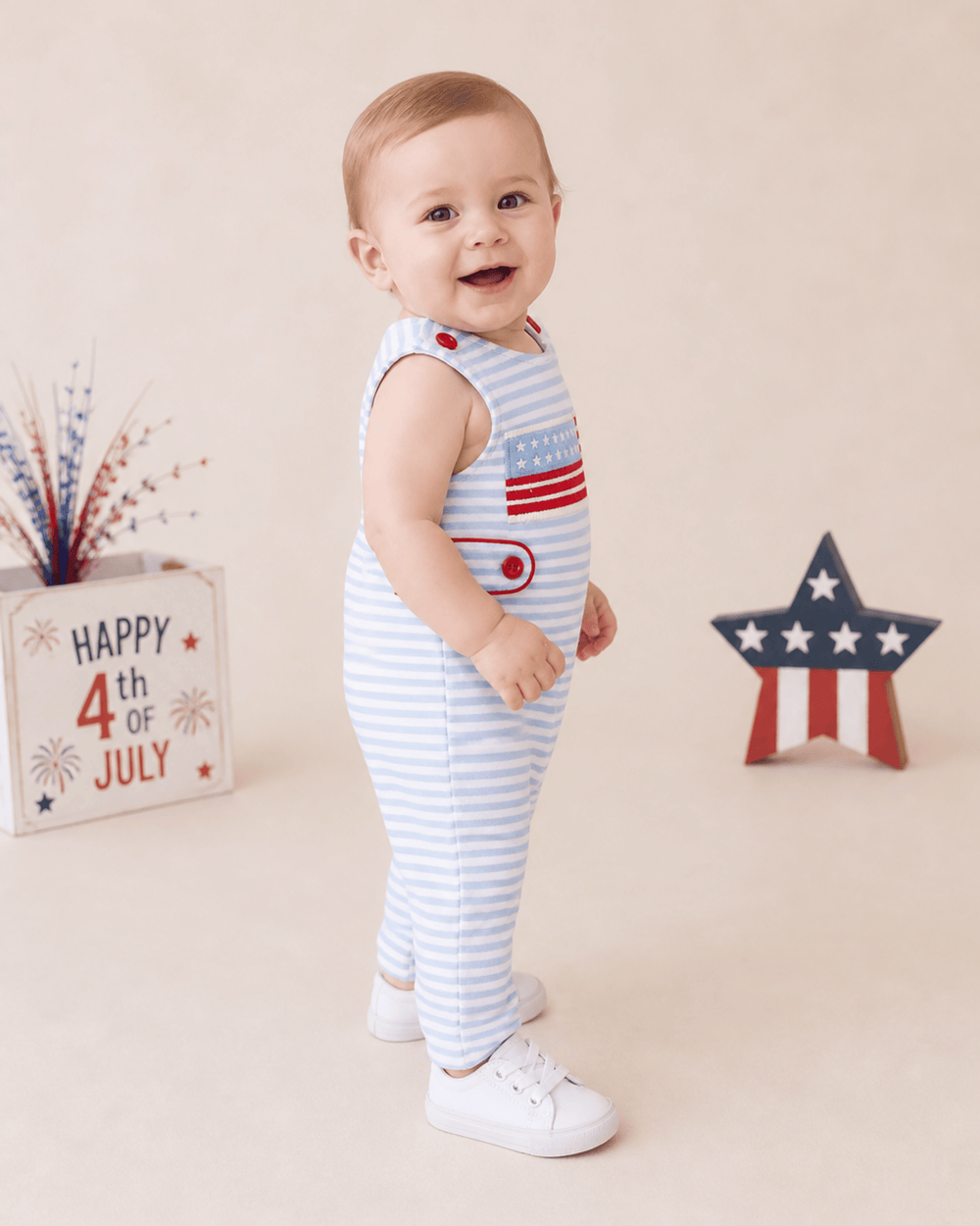 Baby wearing a red, white, and blue outfit with July 4th decorations in the background.