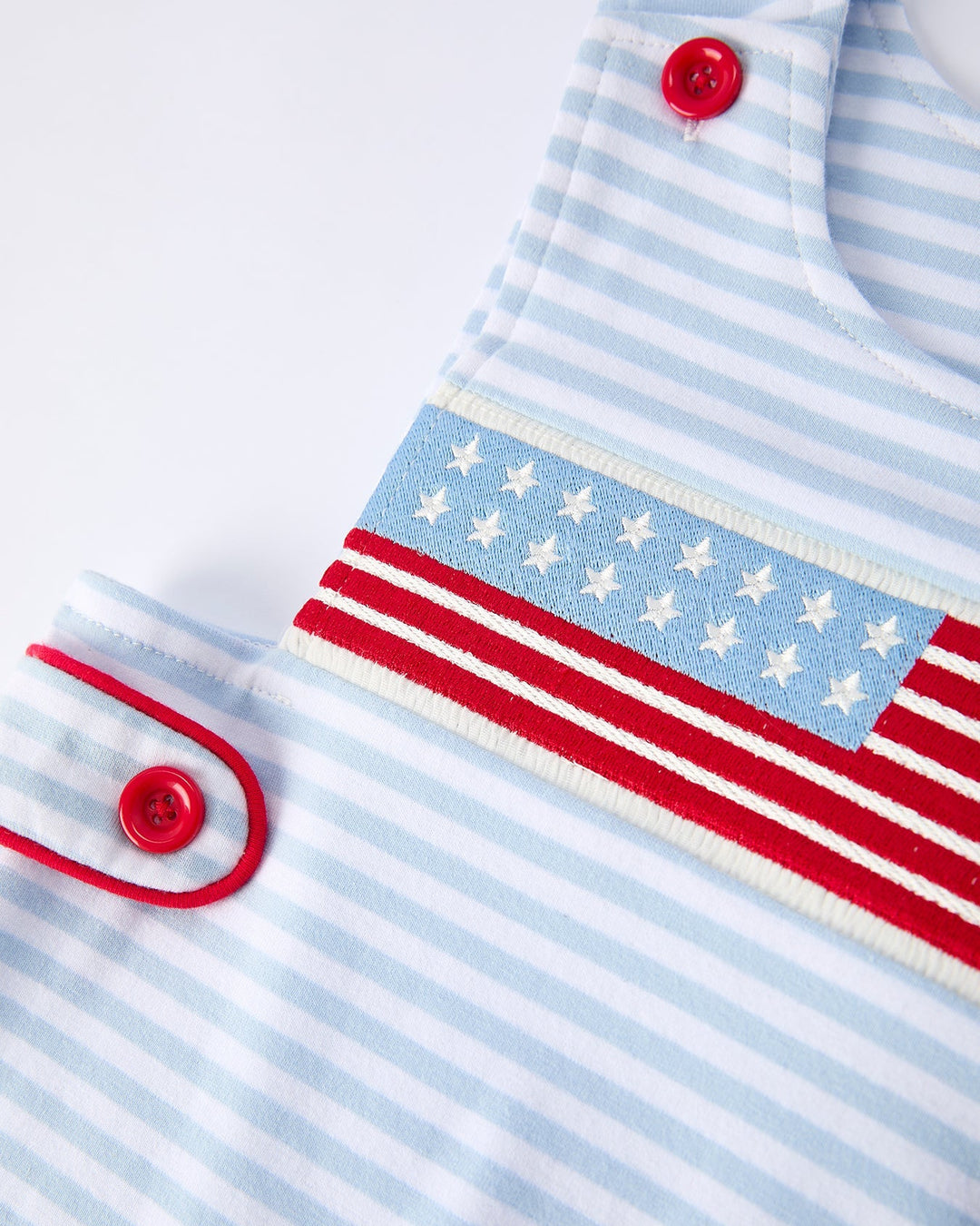 Close-up of a baby outfit with blue and white stripes and red buttons on a light background