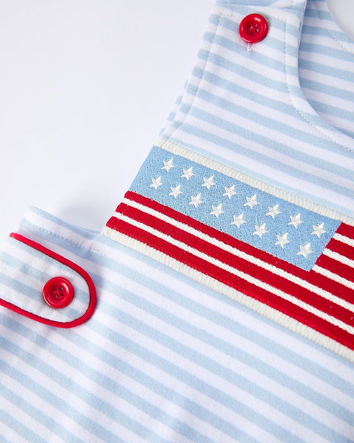 Close-up of a baby outfit with blue and white stripes and red buttons on a light background