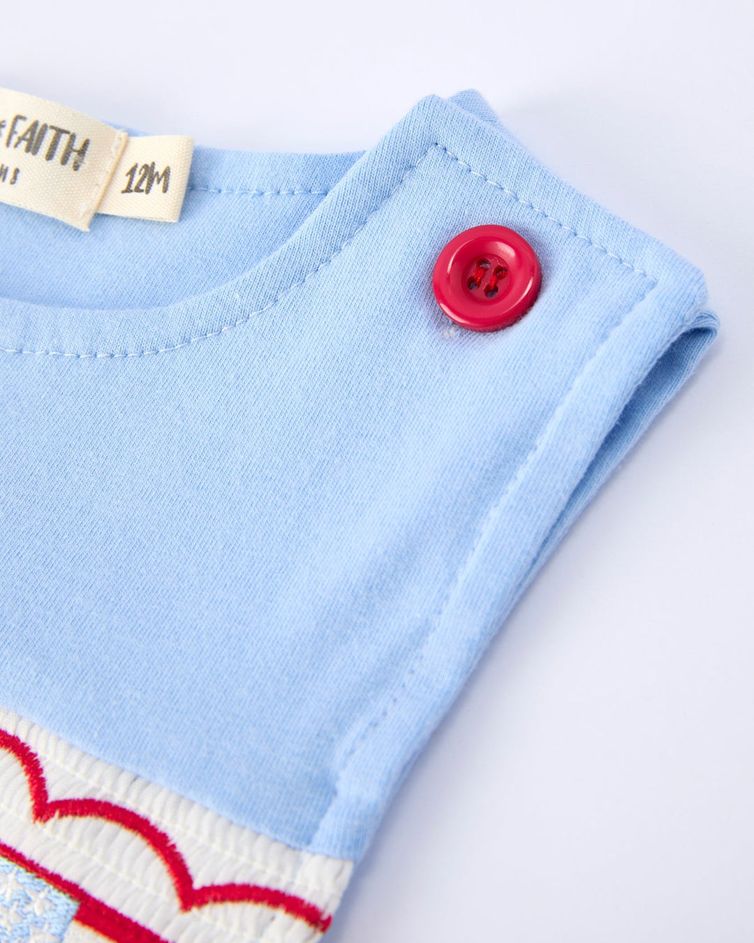 Close-up of a baby outfit with a blue sleeve, red button, and heart pattern on a white background.