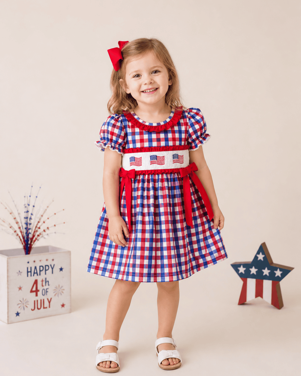 Young girl in a red, white, and blue checkered dress with American flag design, standing in front of a 'Happy 4th of July' sign.