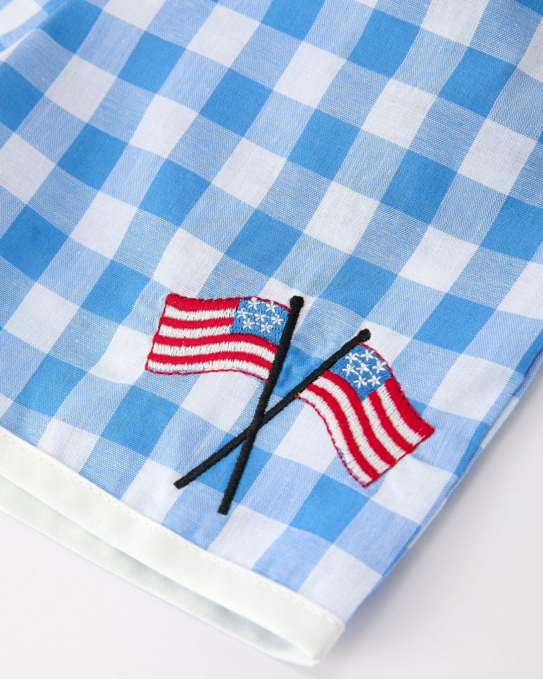 Blue and white checkered fabric with embroidered American flags on a white background