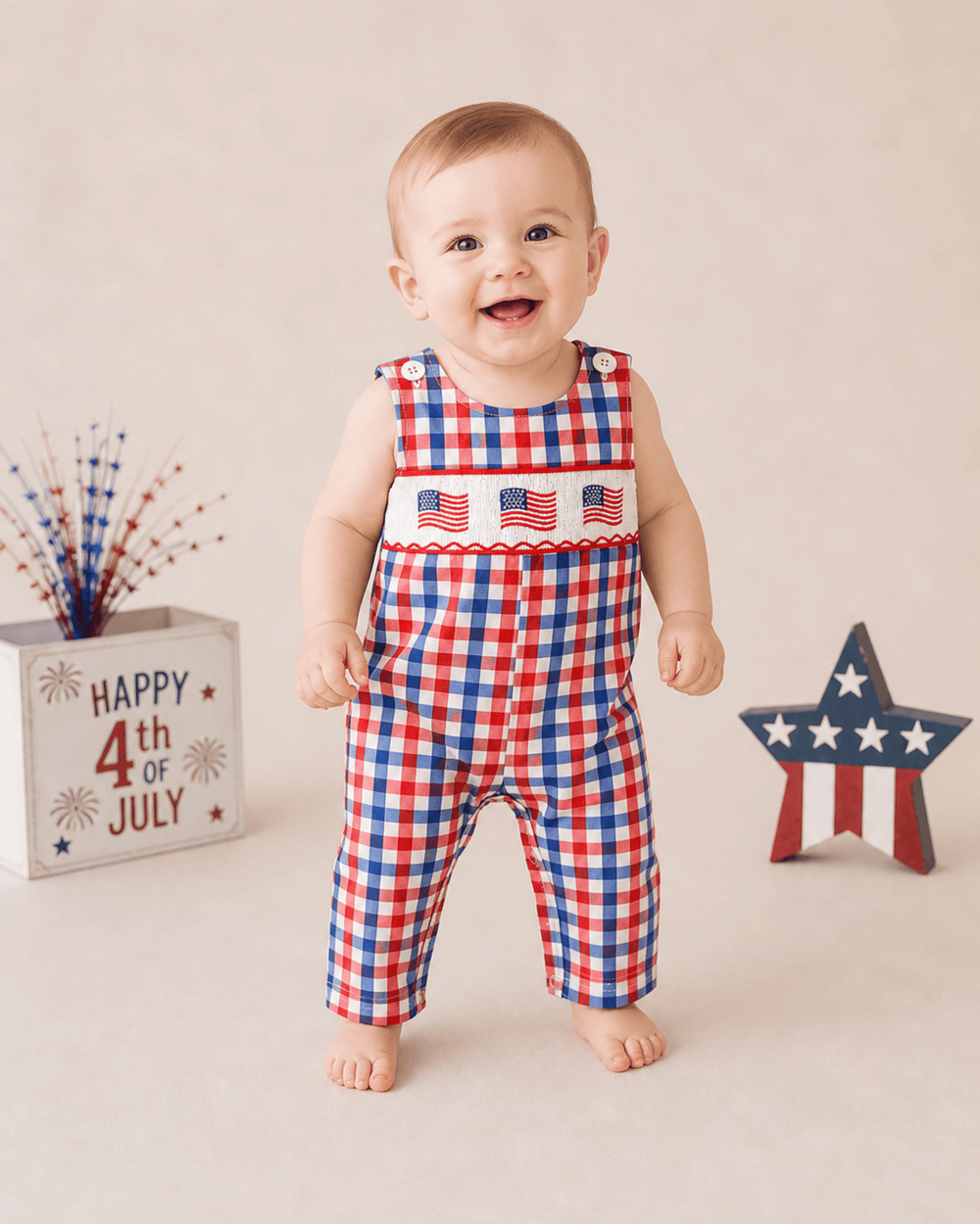 Baby wearing a red, white, and blue checkered outfit with American flag design, standing next to 'Happy 4th of July' decorations.
