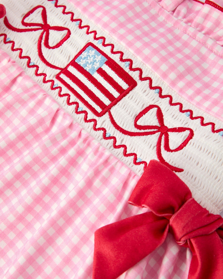 Close-up of a pink checkered dress with red bows and a decorative ribbon.