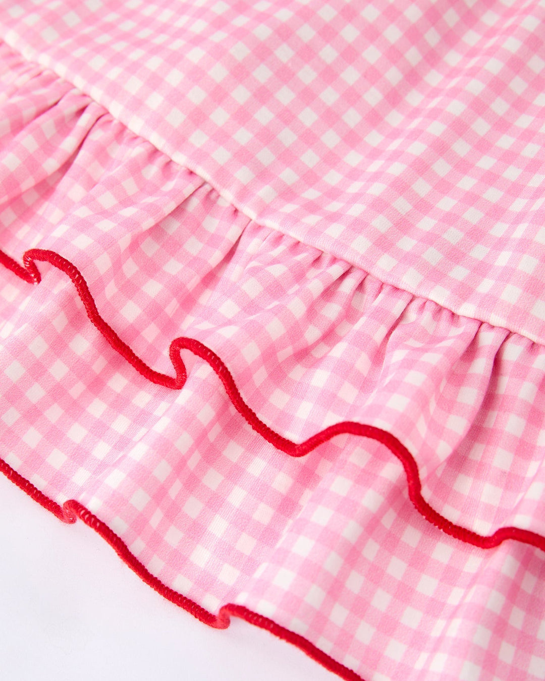 Close-up of a pink gingham fabric with red ruffle trim on a white background