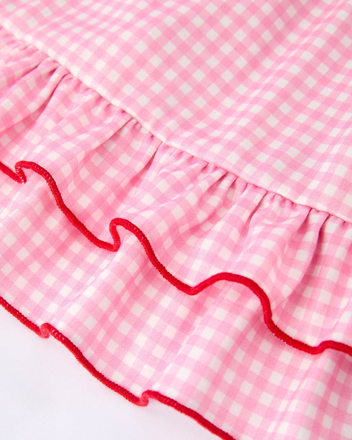 Close-up of a pink gingham fabric with red ruffle trim on a white background