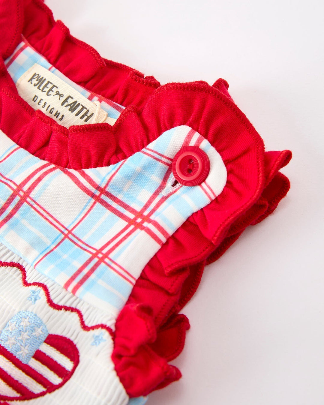 Red ruffled top with plaid pattern and button on a white background