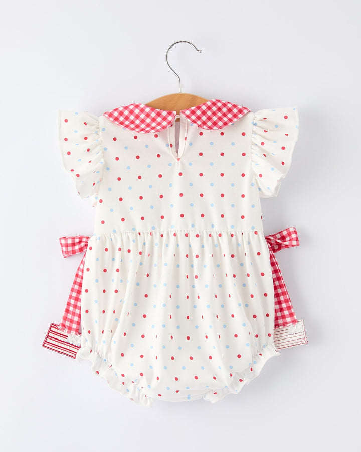 White baby romper with red polka dots and checkered sleeves on a hanger against a white background
