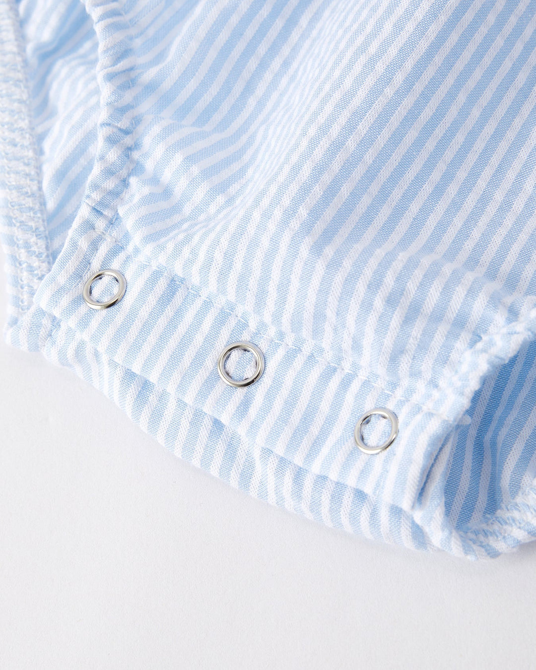 Close-up of a blue and white striped fabric with metal grommets on a light gray background