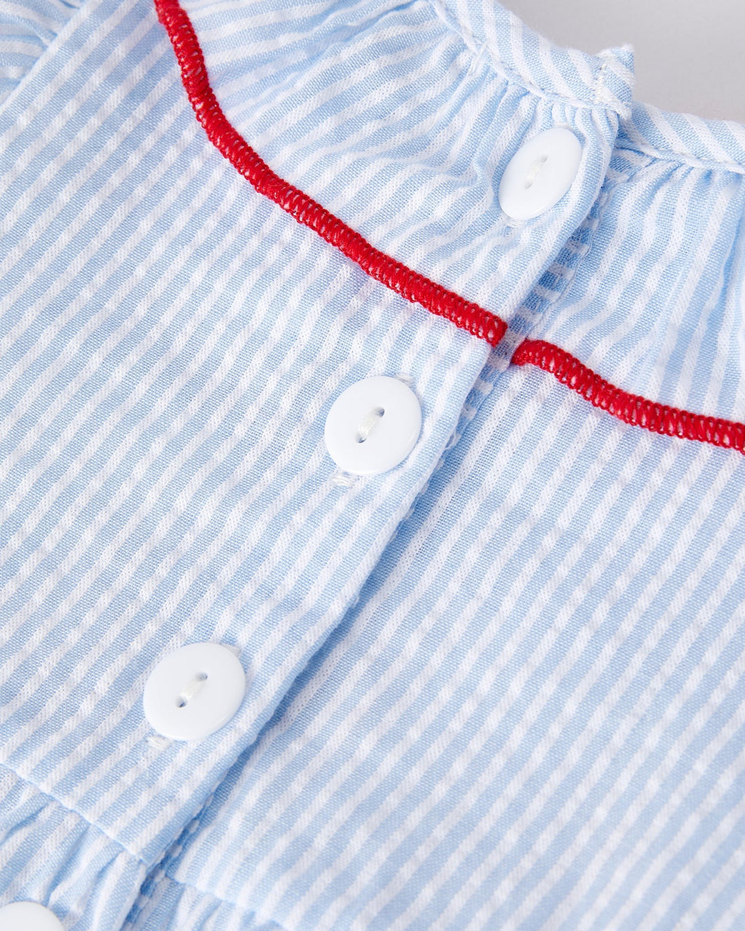 Close-up of a blue and white striped garment with red trim and buttons.