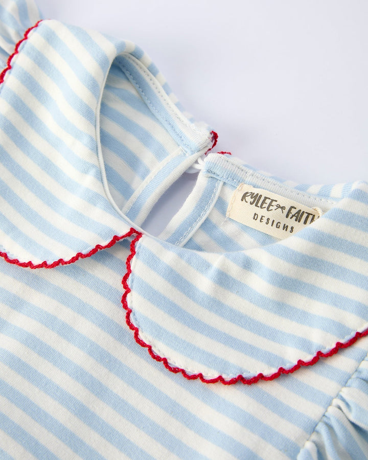 Close-up of a baby dress with blue and white stripes and red trim, featuring a brand label.