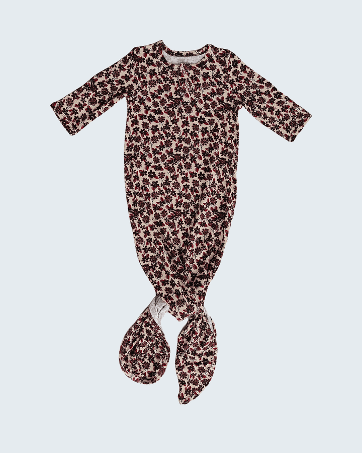 A baby footed sleeper with a brown and black leopard print pattern on a light pinkish-beige base, featuring long sleeves and attached booties at the bottom, shown against a light gray background.