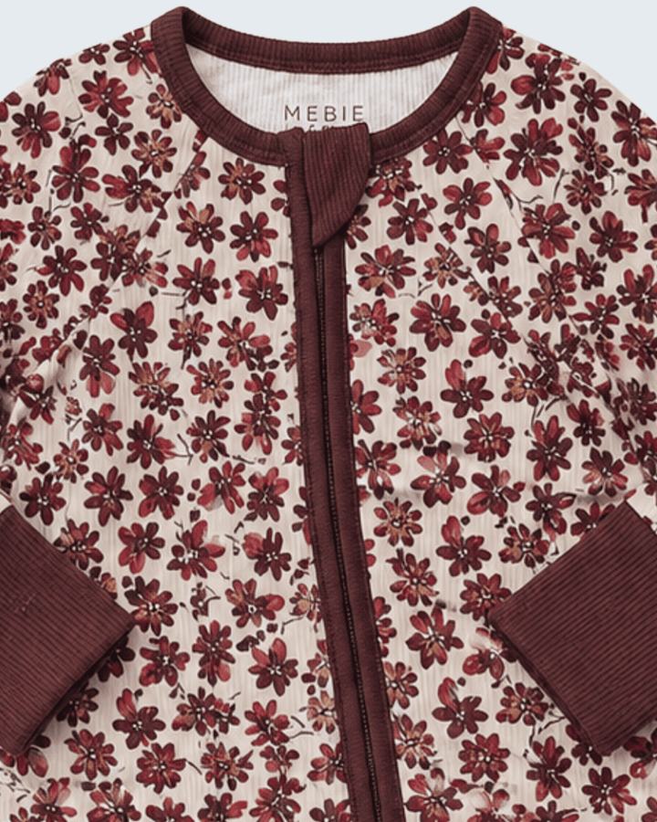 A close-up of a quilted baby cardigan by Mebie Marie, featuring a cream background with a dark red and brown floral pattern, ribbed dark brown trim, and a matching dark brown zipper.