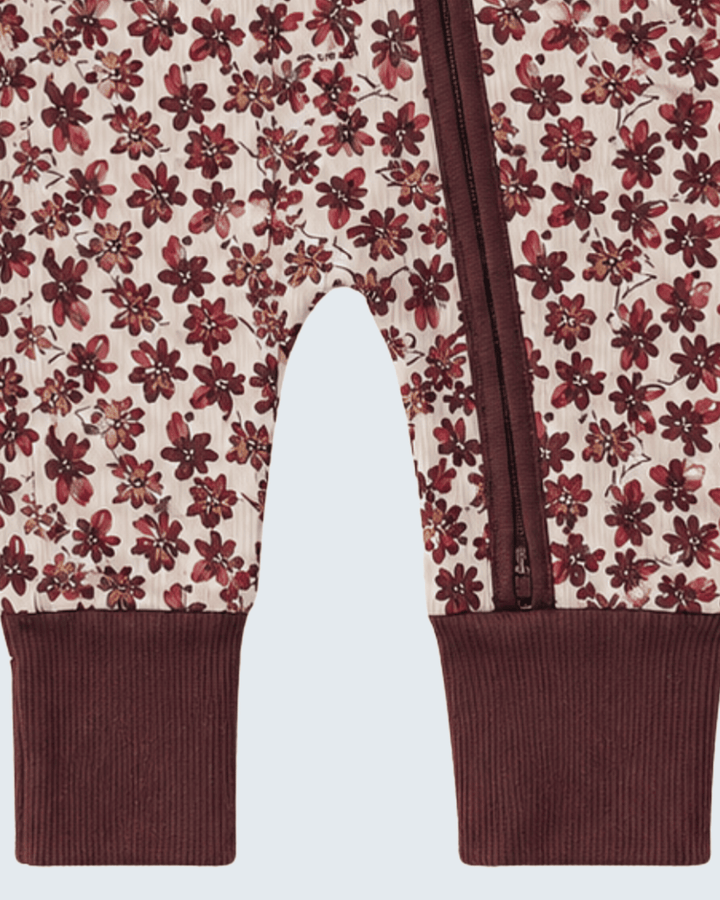 Close-up of a pair of baby pants with an allover floral print in burgundy and dark red on a cream background, finished with solid burgundy ribbed cuffs and a matching zipper.