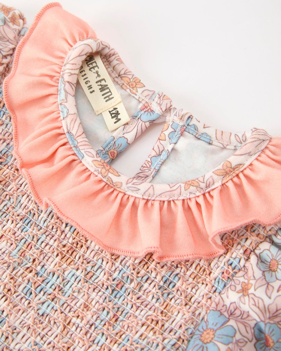 Baby romper neckline close-up: pink ruffle trim, floral print, smocked detail