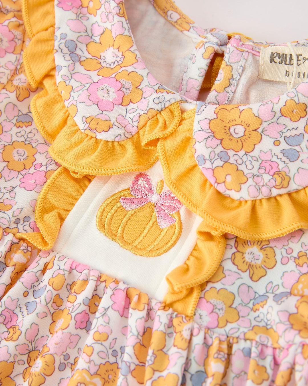 Baby romper detail: pumpkin applique, yellow ruffled collar, pastel floral print