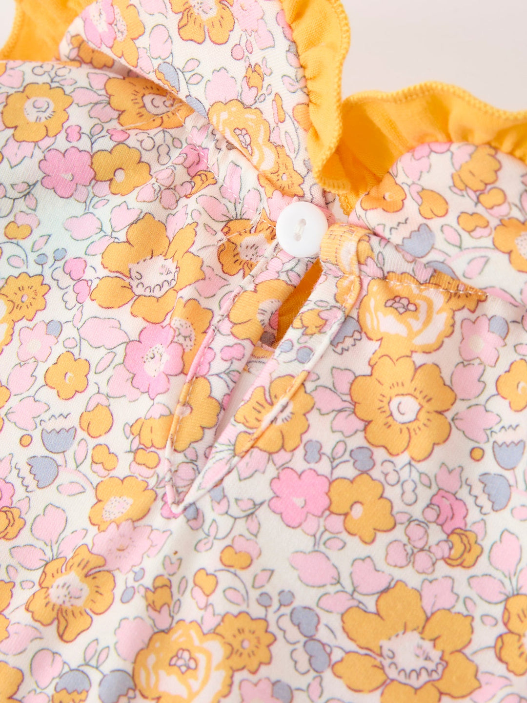 Baby floral romper close-up: yellow trim, button placket, pastel flower print