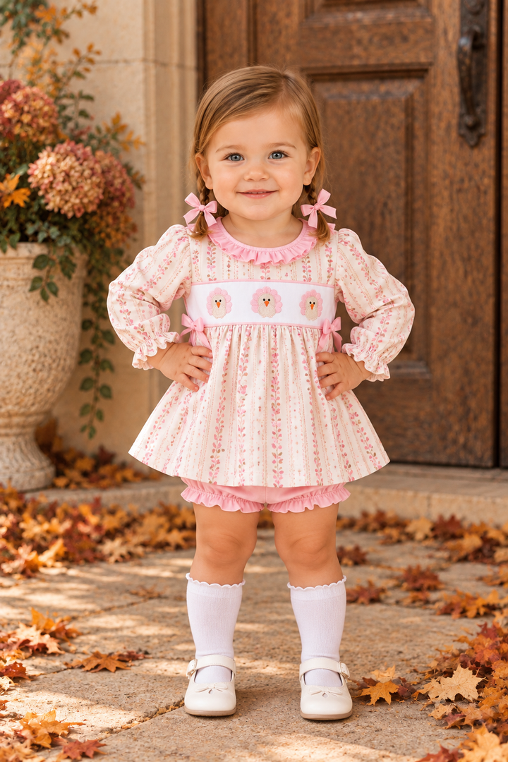 Toddler wearing pink floral ruffle dress with embroidered bloomer shorts and white socks