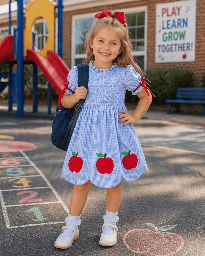 Young girl in a blue dress with red apples standing on a playground.