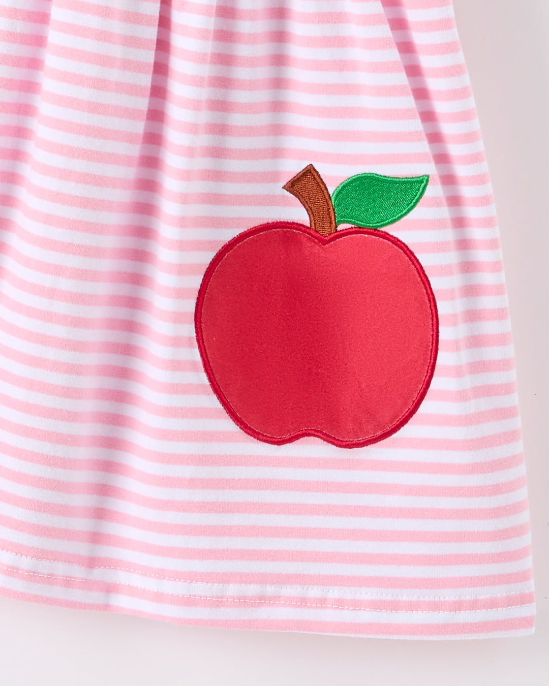 Pink and white striped dress with a red apple applique on a light gray background