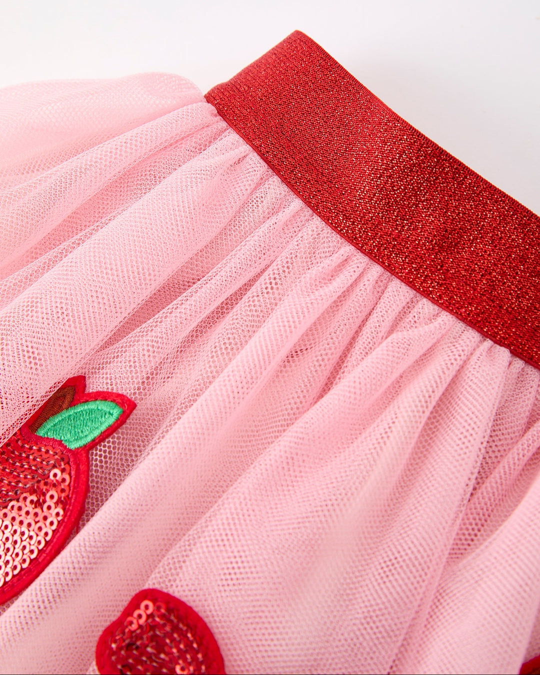 Close-up of a pink skirt with red sequin apples and a red waistband on a white background