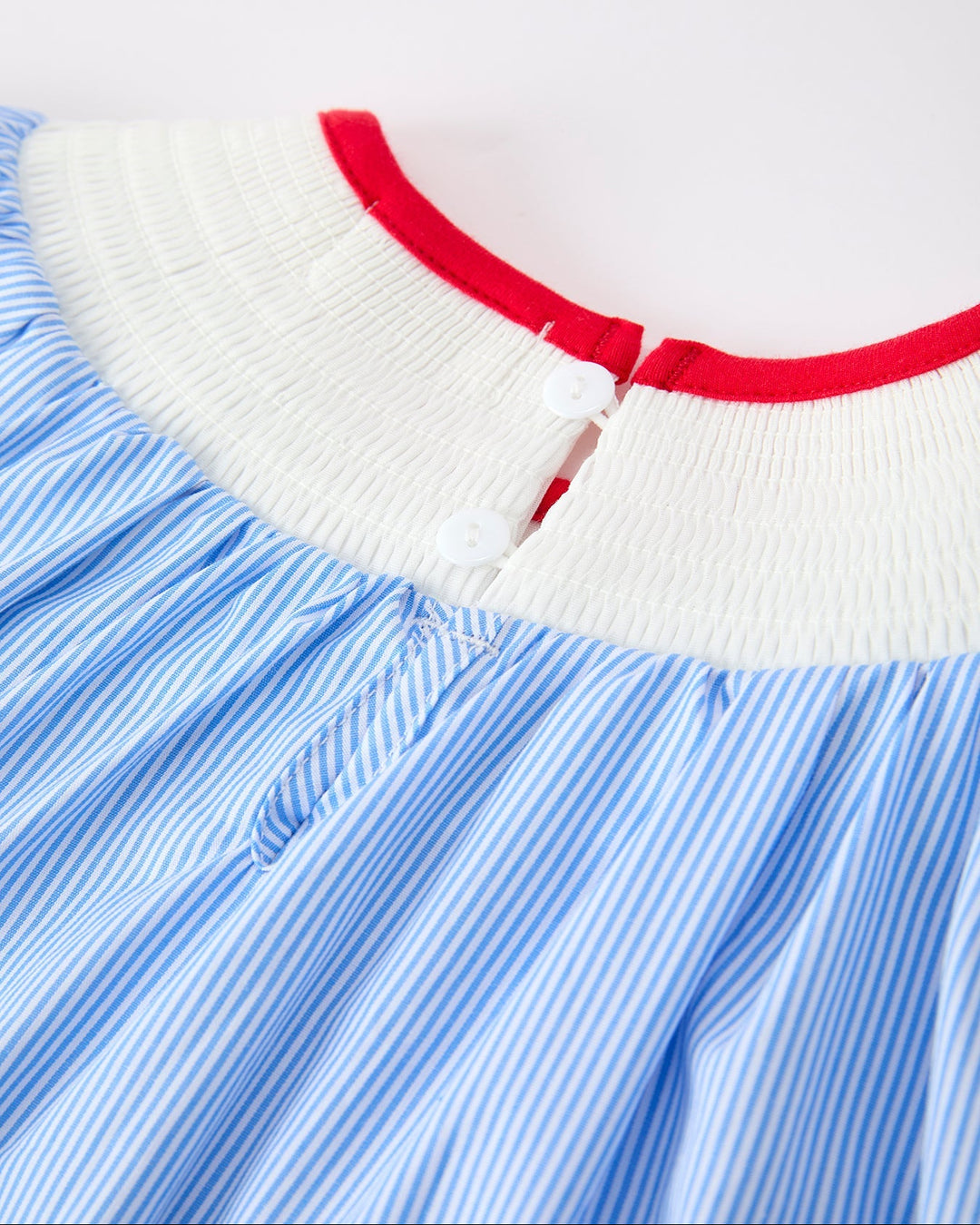 Close-up of a dress with blue and white striped pattern and red trim on a white background