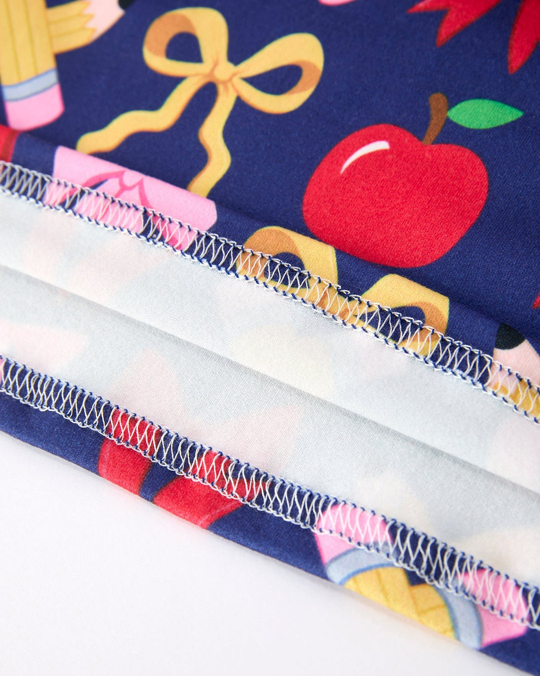 Close-up of fabric with school-themed design including an apple, books, and a bow on a blue background.