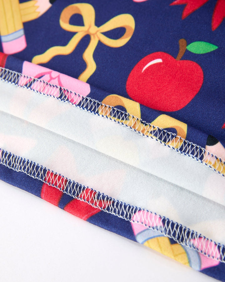 Close-up of fabric with school-themed design including an apple, books, and a bow on a blue background.