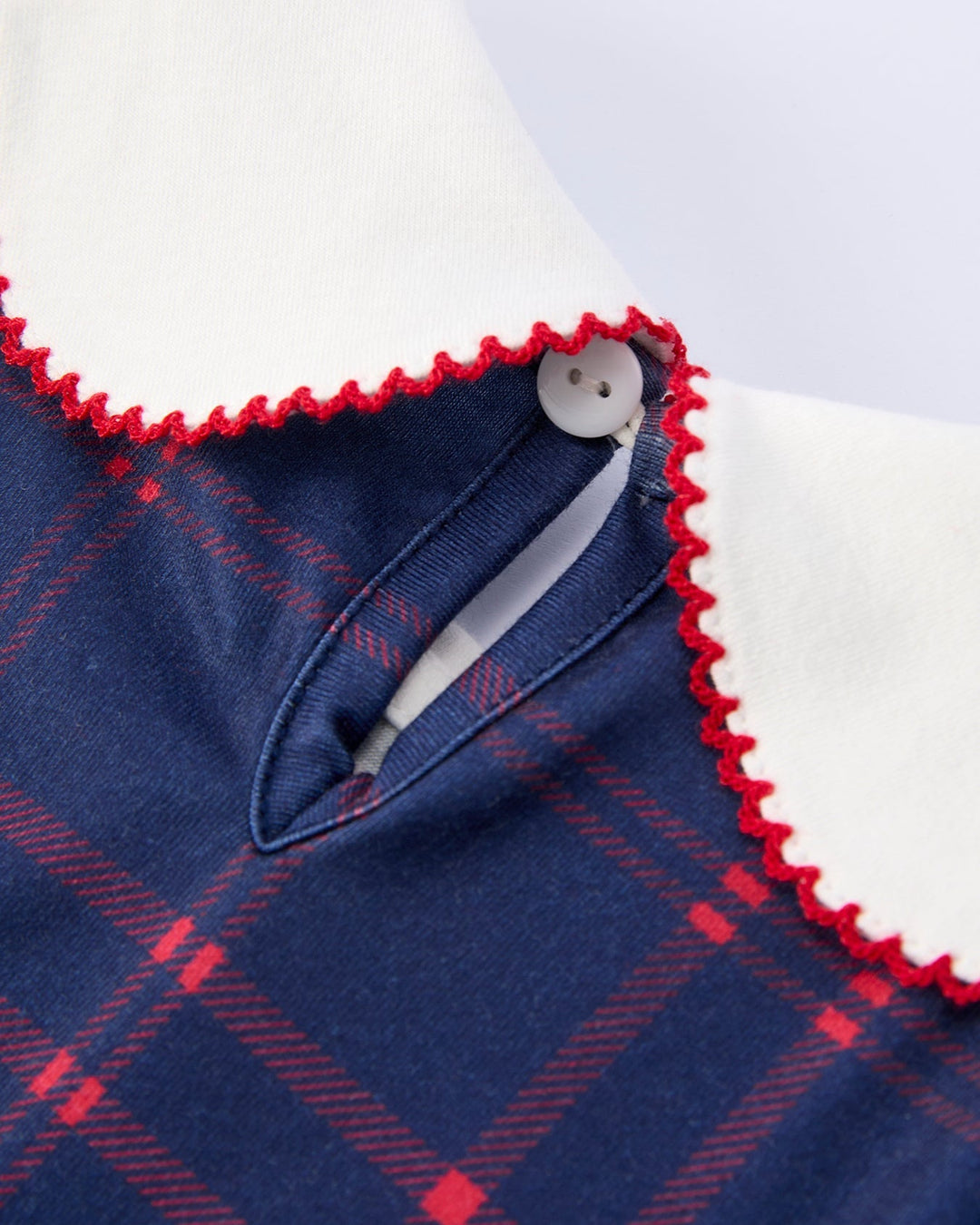 Close-up of a blue plaid garment with white collar and red trim on a light gray background