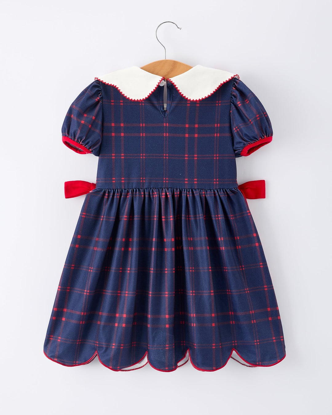 Navy plaid dress with white collar and red accents on a hanger against a white background
