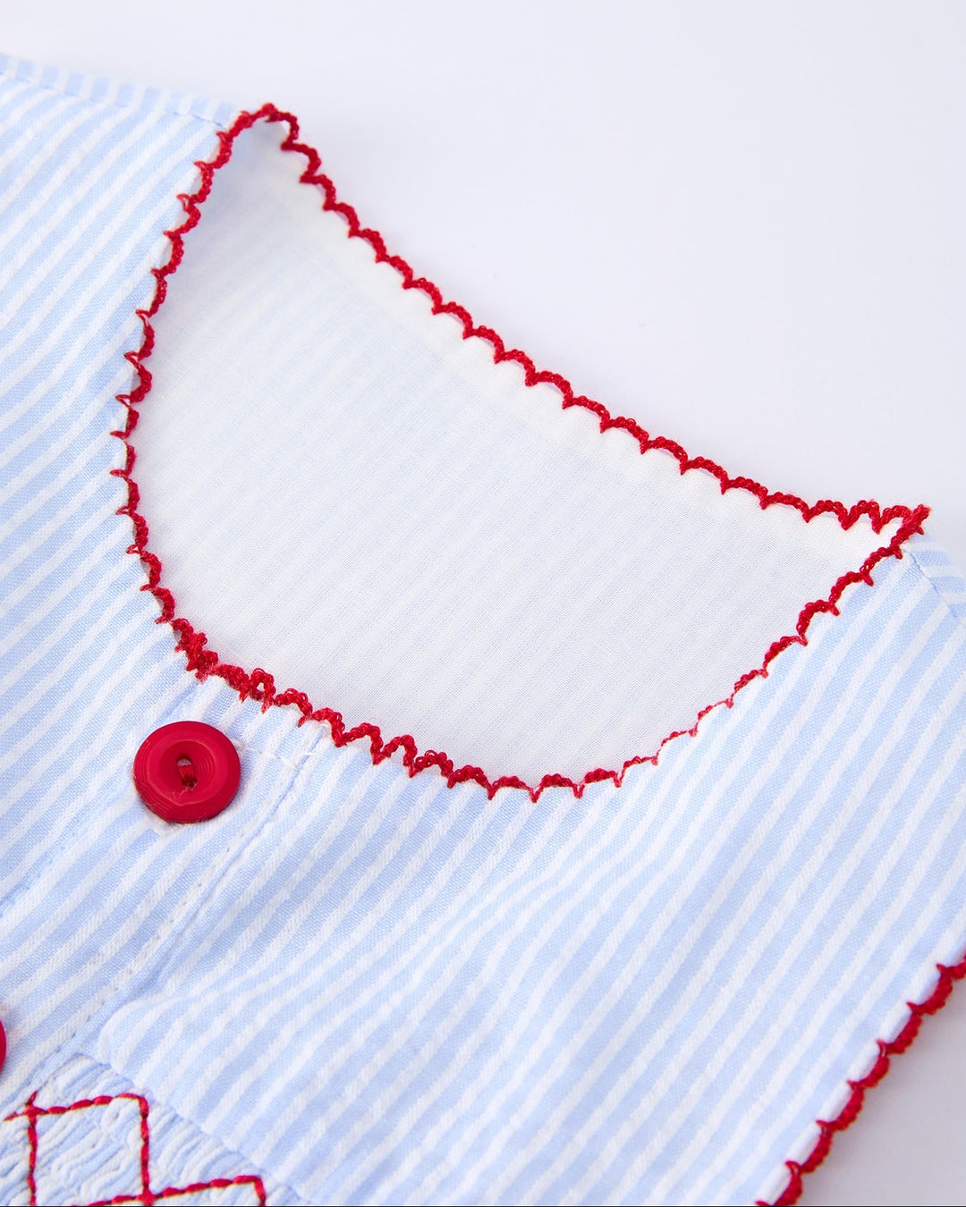 Close-up of a white shirt with red trim and button on a white background