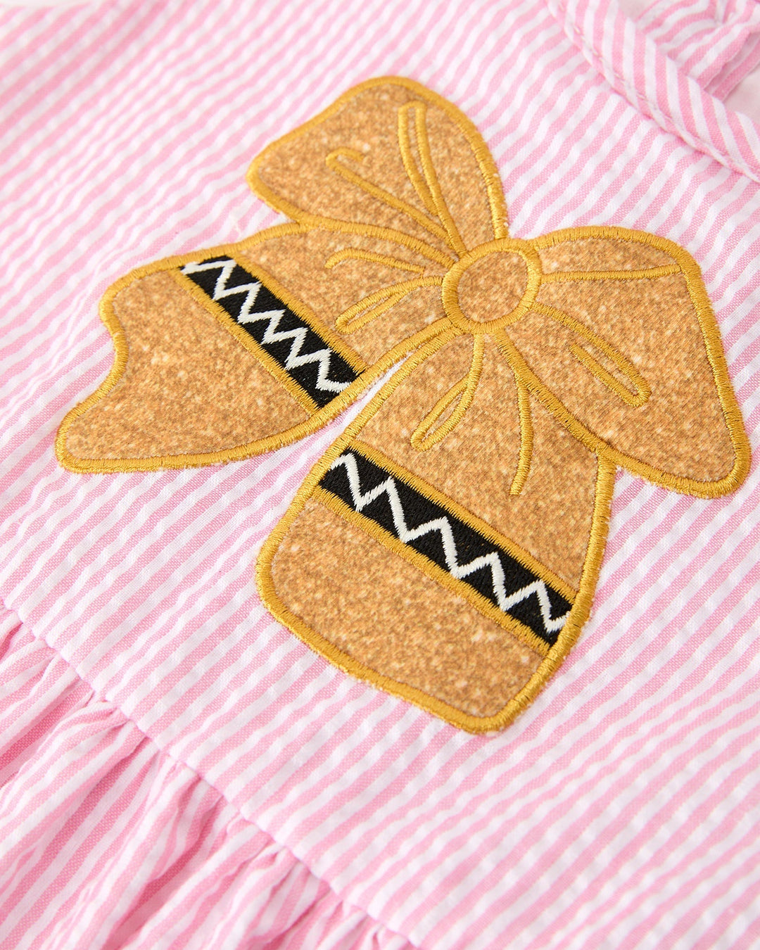 Gold glittery bow patch on a pink and white striped fabric background