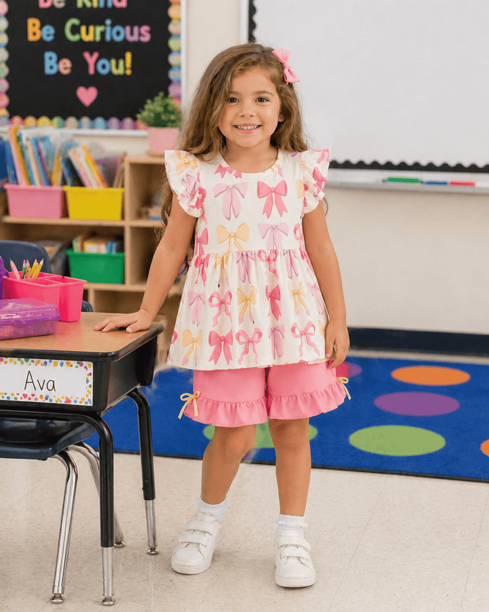 Young girl in a classroom wearing a dress with bow pattern