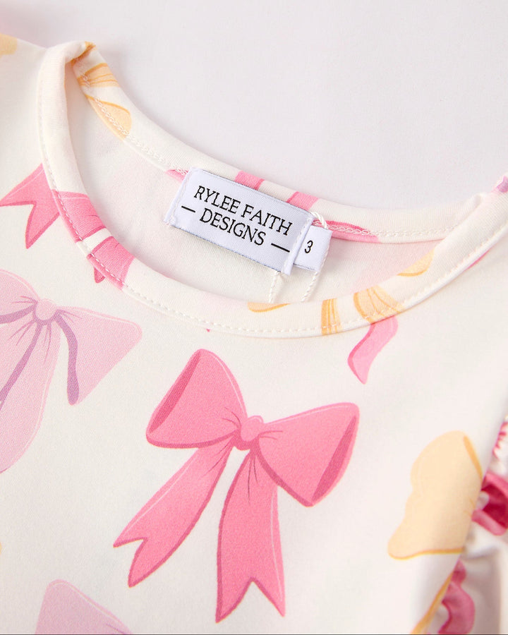 Close-up of a garment with pink bows and a visible brand label on a light background