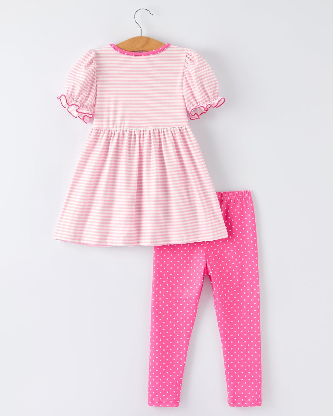 Pink and white striped dress and pink polka dot leggings on a hanger against a white background