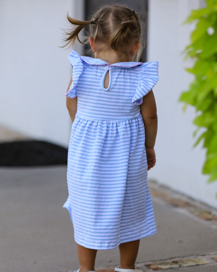 Child wearing a blue and white striped dress with ruffled sleeves, standing on a sidewalk.