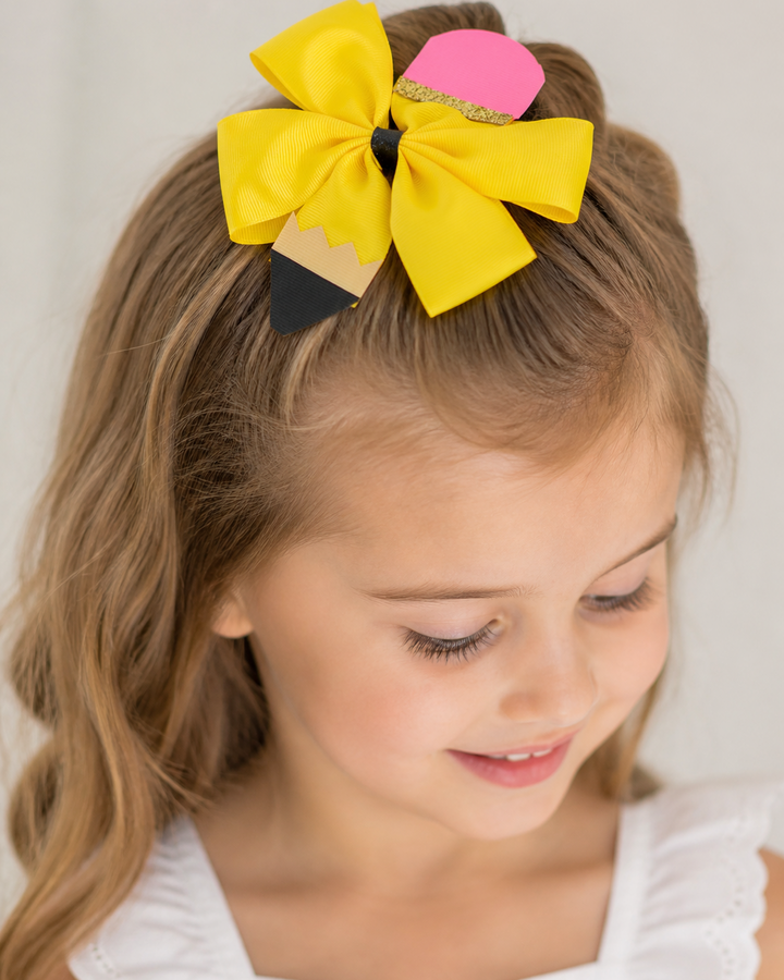 Child with a yellow and pink bow in their hair against a plain background