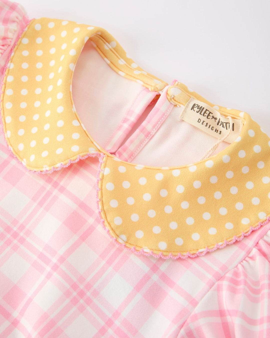 Pink and yellow checkered baby bib with polka dot trim on a white background