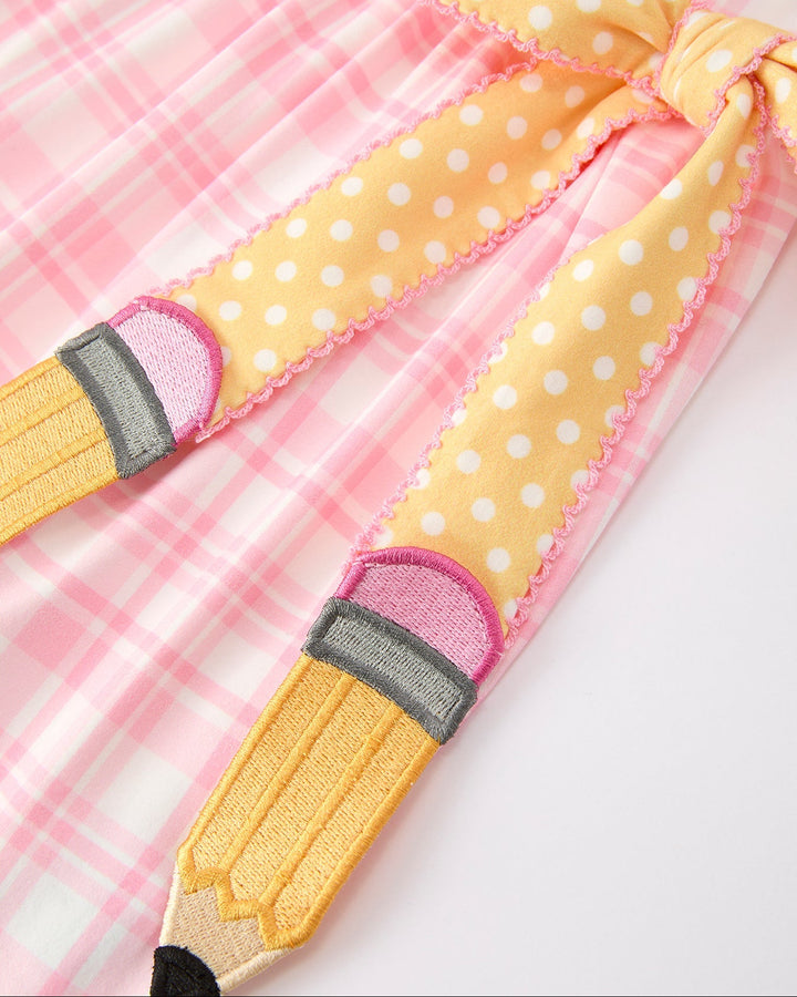 Yellow pencil-shaped toy with polka dot pattern on a pink checkered background