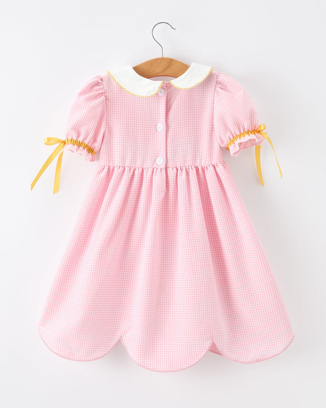 Pink checkered dress with yellow accents on a hanger against a white background