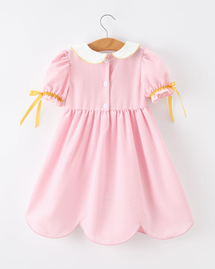 Pink checkered dress with yellow accents on a hanger against a white background
