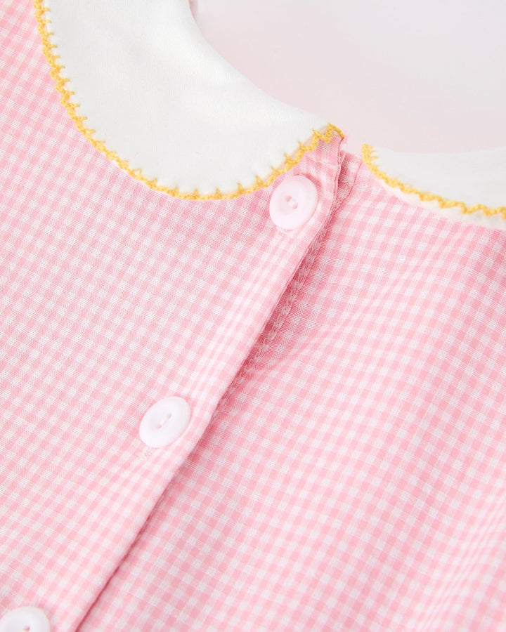 Close-up of a pink gingham dress with white buttons and yellow trim on a white background