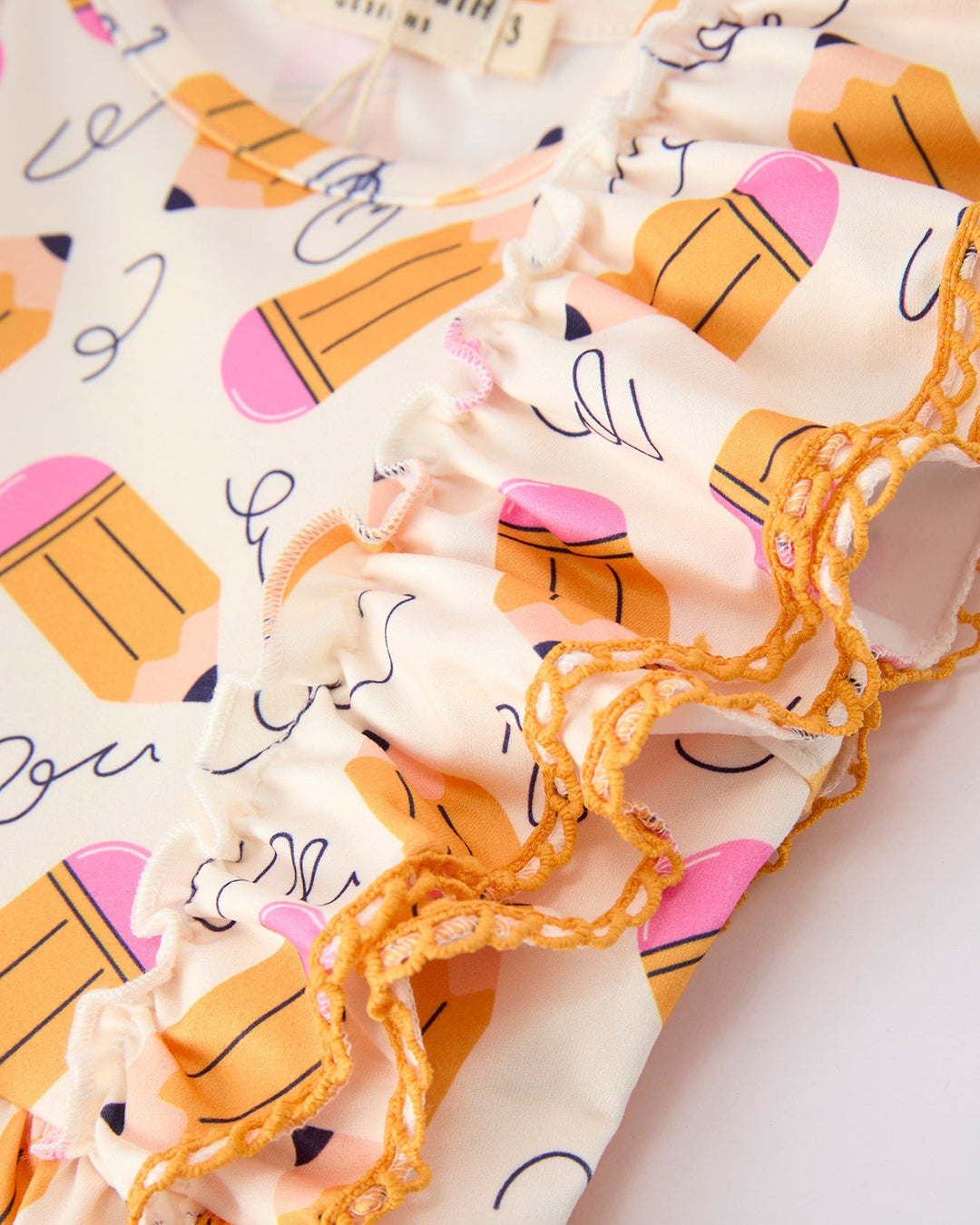Close-up of a fabric with colorful pencil pattern and lace trim.