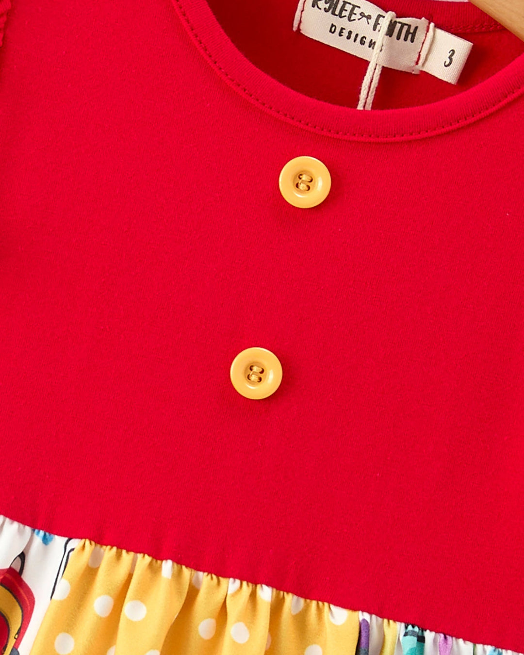 Red top with yellow buttons and colorful skirt, brand label visible